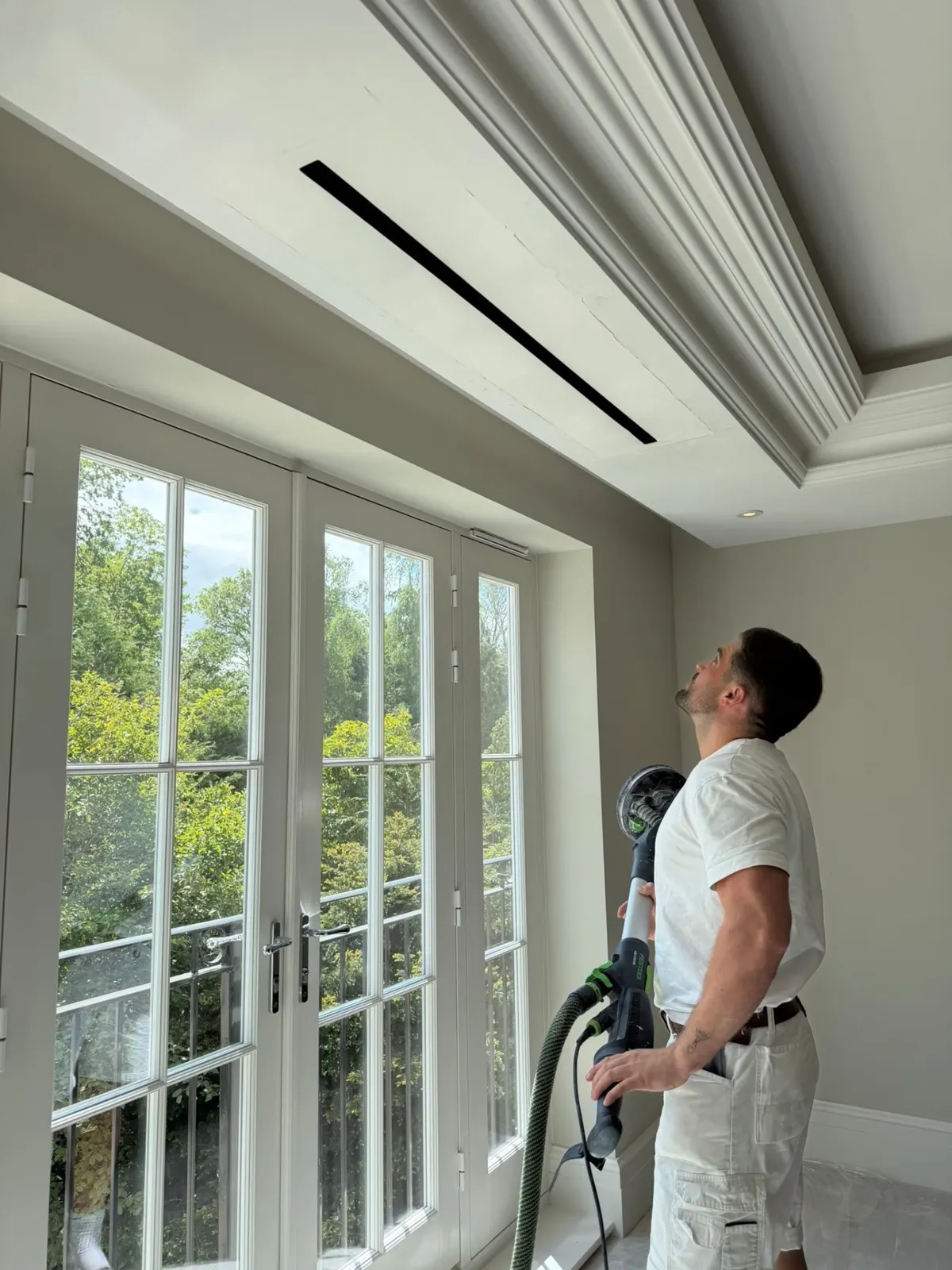 Decorator sanding a ceiling above large glazed doors